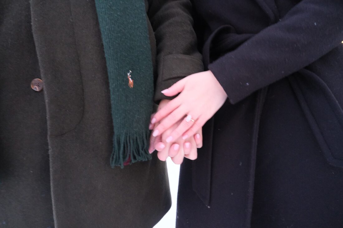 Close-up of their hands clasped together, showing the engagement ring